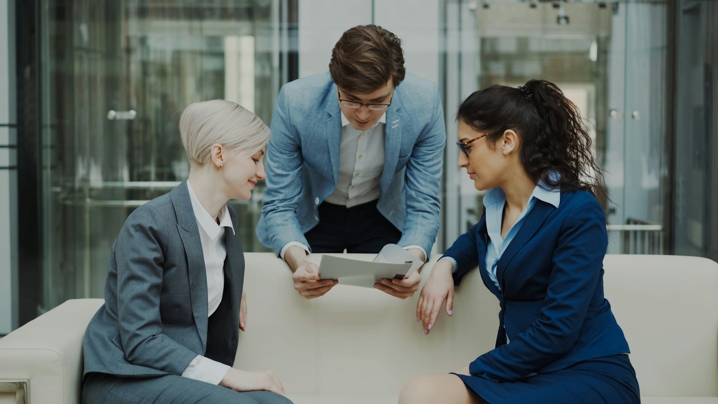 Une équipe d'affaires diversifiée discute de documents sur un canapé de bureau moderne.