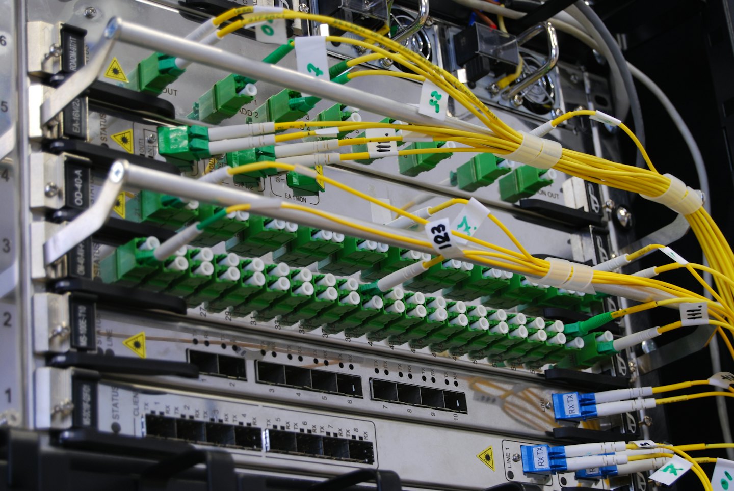 Faisceaux de câbles à fibre optique jaunes connectés à des ports dans une baie de serveurs.